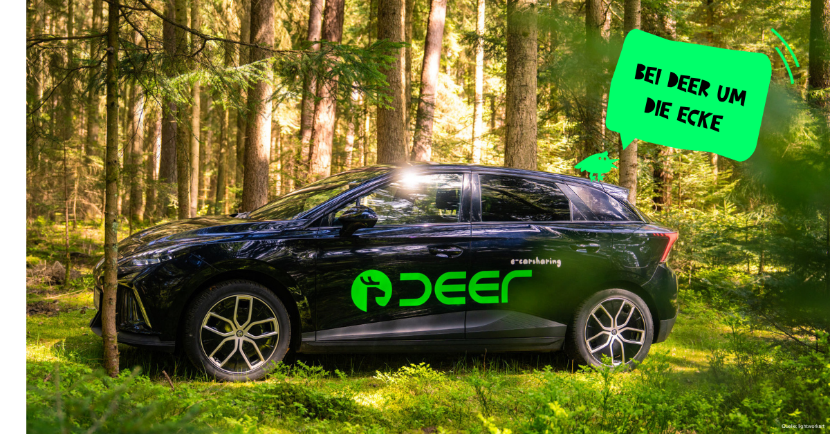 Schwarzes Carsharing-Auto mit grünem „DEER“-Logo im Wald, Sprechblase „Bei Deer um die Ecke“.